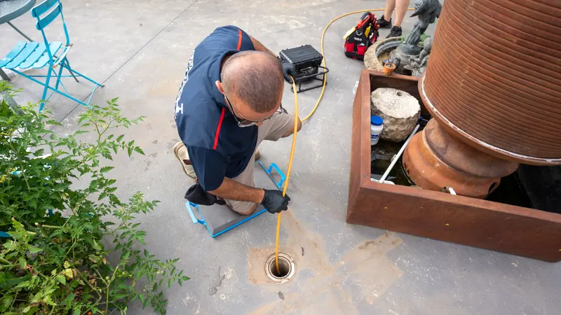 Antons plumber feeding an inspection line into a drain access point beside a rainwater tank