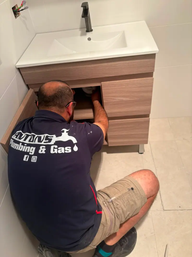 Antons plumbing work on pipe connections underneath a bathroom vanity